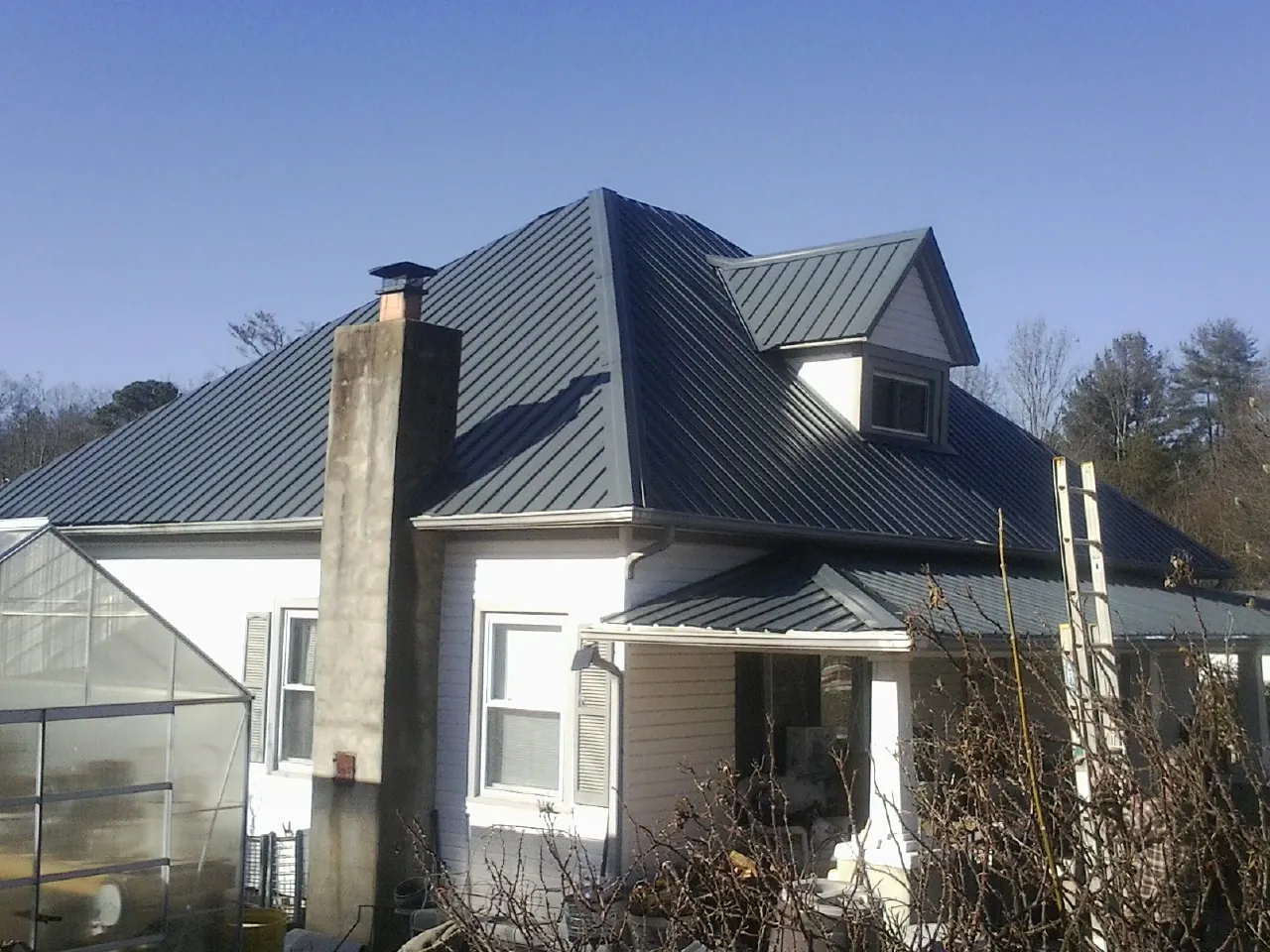 Dark blue standing seam metal roof on a white farmhouse with dormer — Slate & Tile Roof Repair by Roofing Brothers in Wrightsboro