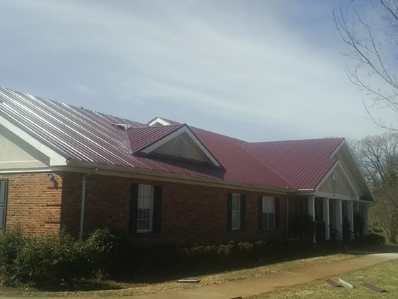 Red metal roof with gabled entries on a long brick building, from a Hail Damage Roof Repair job in Wrightsboro