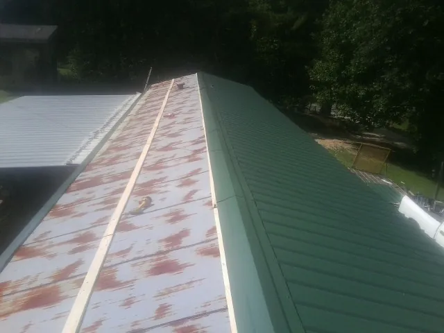 Old rusted panels beside newly installed green metal roofing — Wind Damage Roof Repair by Roofing Brothers in Wrightsboro