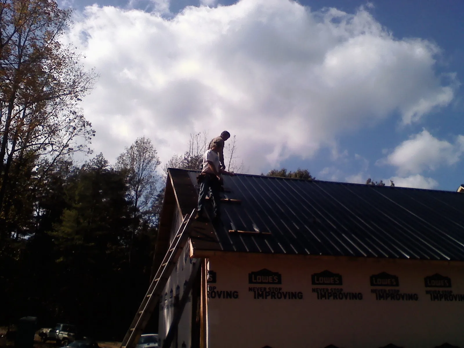 Roofer fastening dark metal panels high against a cloudy sky, from a Roof Inspection job in Wrightsboro