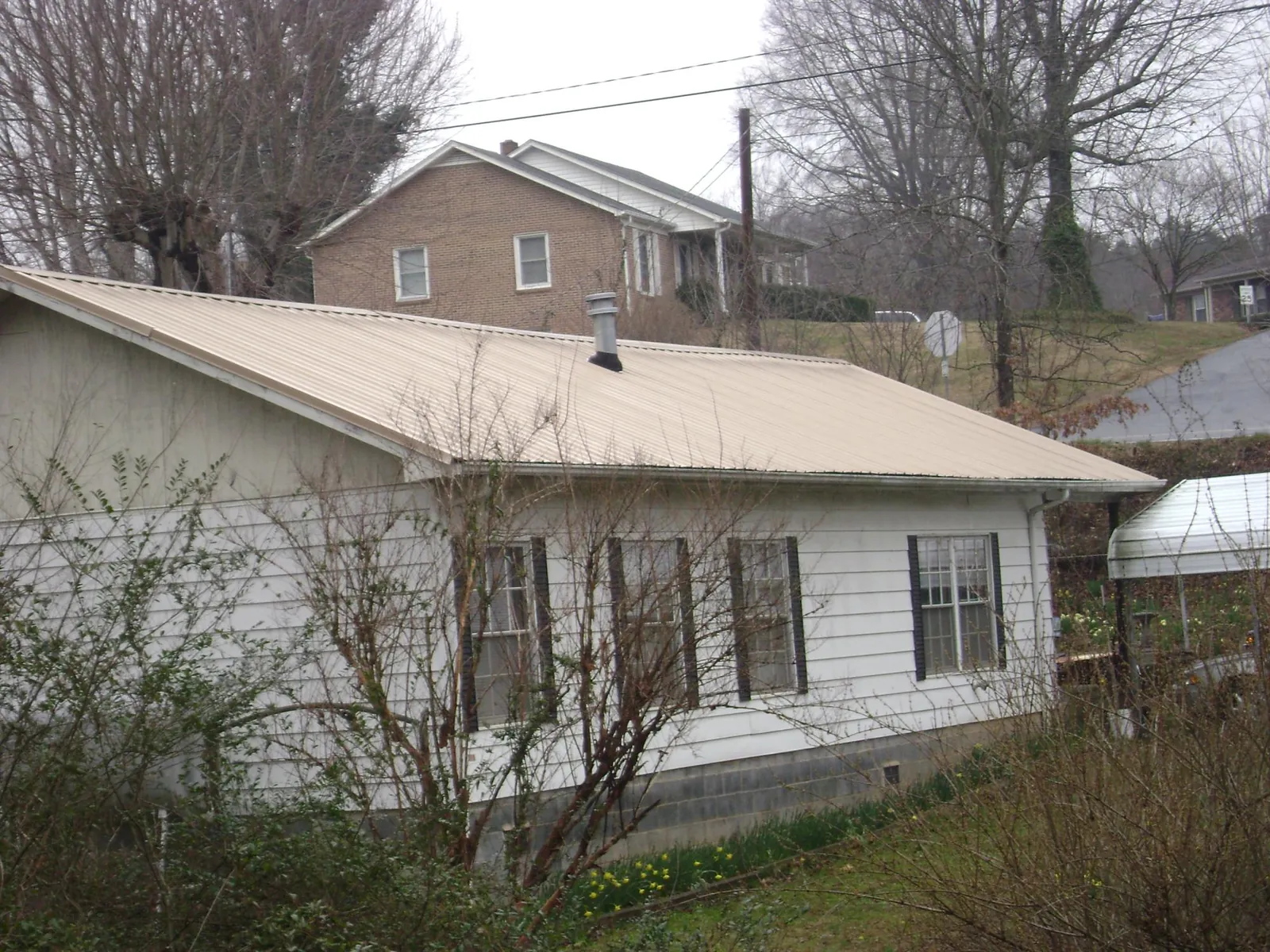 Tan metal roof on a white sided house set into a hillside — Commercial Roofing by Roofing Brothers in Wrightsboro